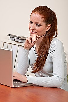 Long red hair woman at office holding glasses working with computer