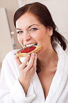 Young woman in bathrobe eating toast for breakfast in kitchen