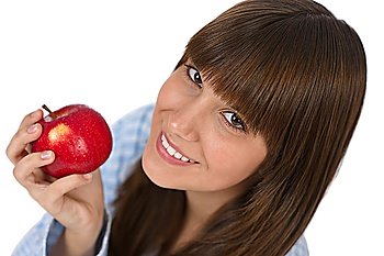 Happy teenager in pajamas eating healthy apple for breakfast on white background