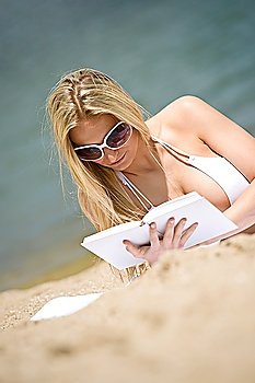 Blond woman reading book on sunny beach