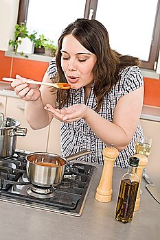Cook - plus size woman tasting Italian tomato sauce in modern kitchen