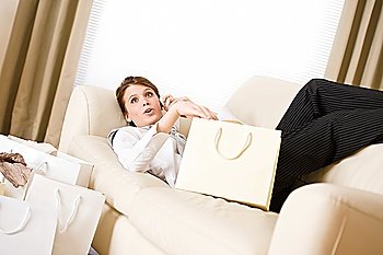 Young business woman lying down on sofa with luxury shopping bag, on the phone calling