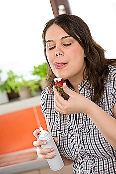 Plus size woman with whipped cream on strawberry licking lips in kitchen