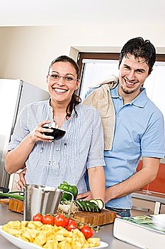 Cheerful couple in modern kitchen cook together, drink red wine