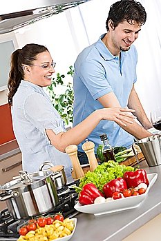 Smiling couple cooking in modern kitchen with vegetable and pasta