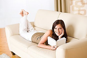 Young happy woman read book on sofa in living room