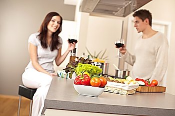 Young couple drinking red wine in kitchen, focus on bowl with vegetable