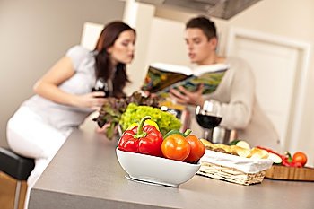 Young couple in kitchen choosing recipe from cookbook drinking red wine