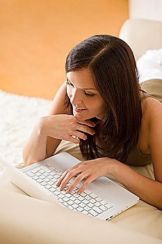 Young woman with laptop lying down on sofa home in living room