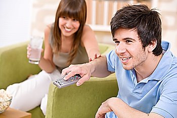 Student - happy teenagers watching television holding remote control in living room