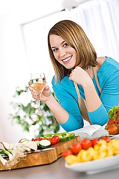 Cooking - Smiling woman with glass of white wine in kitchen with pasta and vegetable