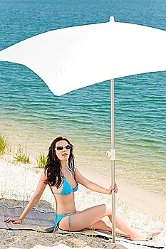 Summer woman in bikini alone on beach sunbathing under parasol