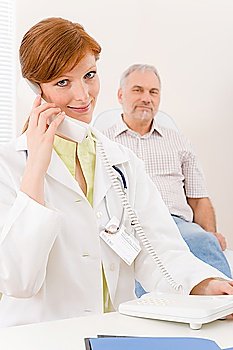 Doctor office - portrait female physician make phone call, senior patient in background