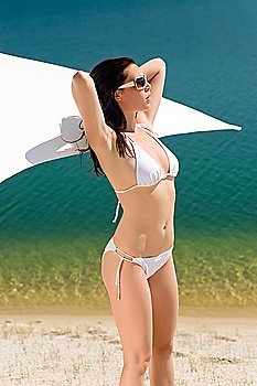 Young sexy bikini model posing with sunglasses by beach parasol