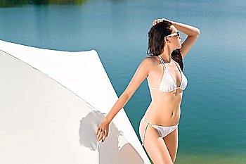 Young sexy bikini model standing with sunglasses by beach parasol