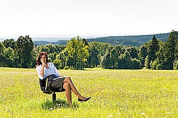 Young businesswoman sitting armchair outside in middle of sunny meadow