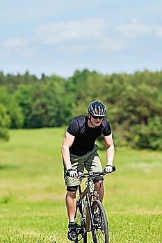 Fit young man cycling uphill mountain bike in summer coutryside
