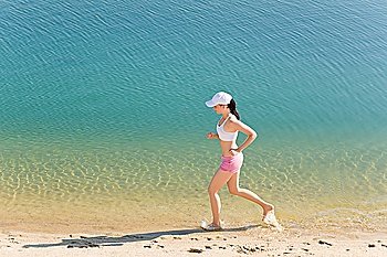 Summer active woman jogging on beach seashore in fitness outfit