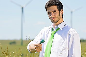 Green energy - young businessman hold plug in field with windmill