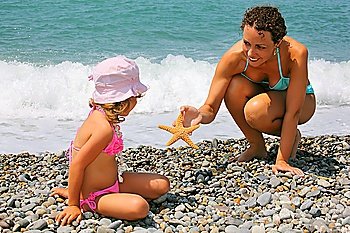 young woman gives starfish to little girl on stony beach
