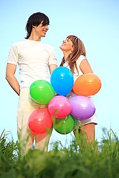 girl and guy stand in grass with multicoloured balloons