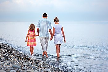 Happy family with little girl walk on beach in evening