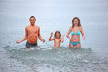 Happy family with little girl splashes water hands standing on belt in sea