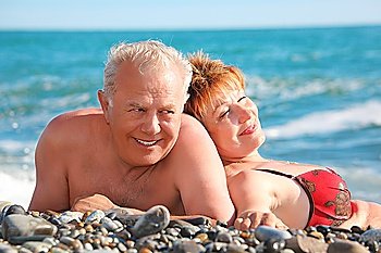 happy aged pair lie on pebble beach