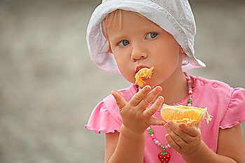 little girl wearing panama hat is eating orange. focus on right hand.