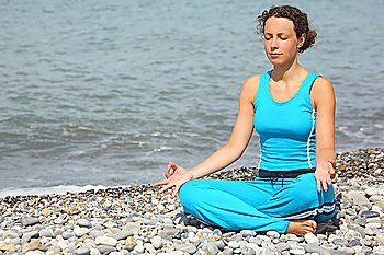 joyful woman wearing sporty clothers is meditate on a sea coast.