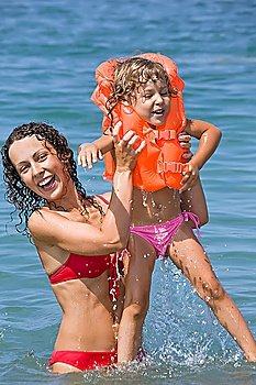 young woman keeps in hands little girl in lifejackets in sea on resort