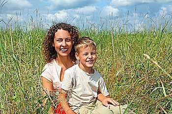 young woman and smiling boy sitting on meadow