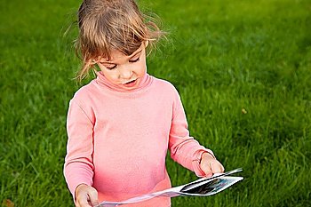 girl stands on green grass field. girl reds looks considers book tale. girl looks in book portrait