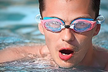 young man in watersport goggles swimming in pool, taking breath