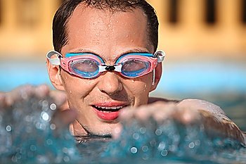 young man in watersport goggles swimming in pool, extended hands forward
