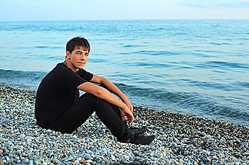sitting teenager boy on stone seacoast near sea