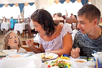 young caucasian family having dinner together. mother, father and daughter in cafe. mum feeds girl from plug
