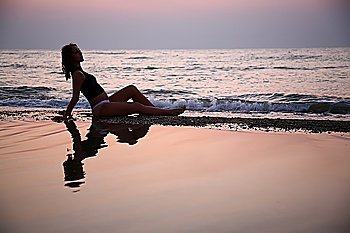 Young woman seats in water on beach on sunset