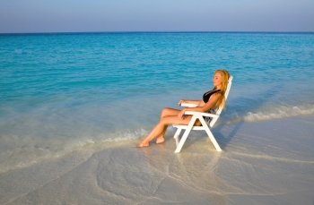 Young pretty woman tans in beach chair, it put in ocean