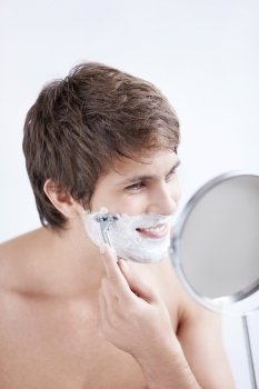 Young man shaving at the mirror on a white background
