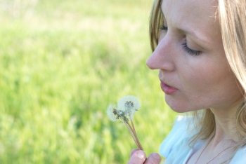 Pretty blonde girl with dandelion on the green field