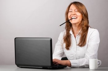 business woman is sitting in the office with laptop and working with pencil in her teeth