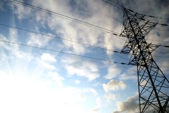 electrical tower with bright sun, blue sky and white clouds