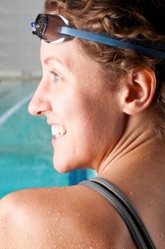 portrait of a woman swimmer looking at camera with blurred swimming pool behind her