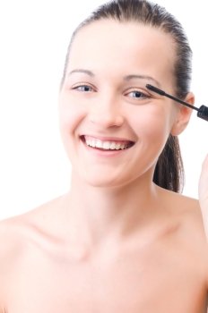 young smiling woman is applying mascara on her face and looking at camera, isolated on white