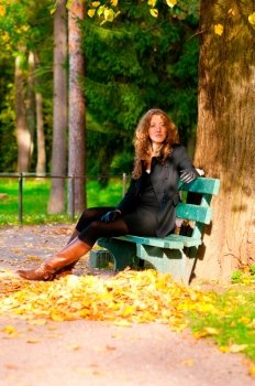 young woman is sitting on the bench in autumn park and looking at camera