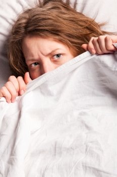 angry woman is lying in bed under blanket and doesn´t want to wake up