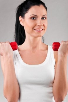 sporty woman is holding barbells on grey background
