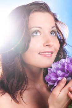 beautiful woman with flower is looking at camera on blue background