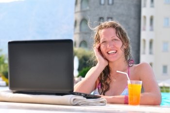 beautiful woman is using laptop at poolside and looking at camera